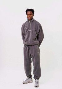 Grau gefütterter Trainingsanzug mit hohem Kragen, Reißverschluss und elastischem Bund. Ergänzt durch graue Sneaker für einen kompletten Look.