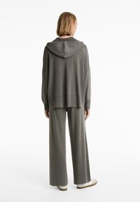 Grå stickad hoodie med ribbat mönster och oversized passform som matchas med vida byxor. Försedd med en justerbar huva.