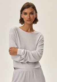 Jasnoszary, prążkowany sweterek z długimi rękawami i okrągłym dekoltem, charakteryzujący się luźnym krojem i delikatną teksturą.