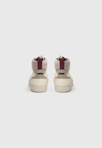 Een paar beige high-top sneakers met gevoerde mesh kraag en bordeauxrode trekbanden, gezien vanaf de achterkant op een witte achtergrond.