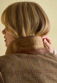 Hnedá károvaná bunda s vysokým golierom, ktorá má béžový kožený akcent. Na golieri je razený nápis "JOULES". Hladká štruktúra, strih na mieru.