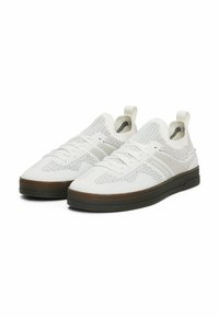 Zapatillas deportivas blancas hechas de malla transpirable, con un diseño texturizado, cierre de cordones y una suela de goma oscura contrastante.