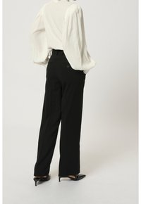 Zwarte wijde broek van gestructureerde stof, met een hoge taille, zijzakken en twee knopen achter. Witte textuur blouse met opgezette mouwen.