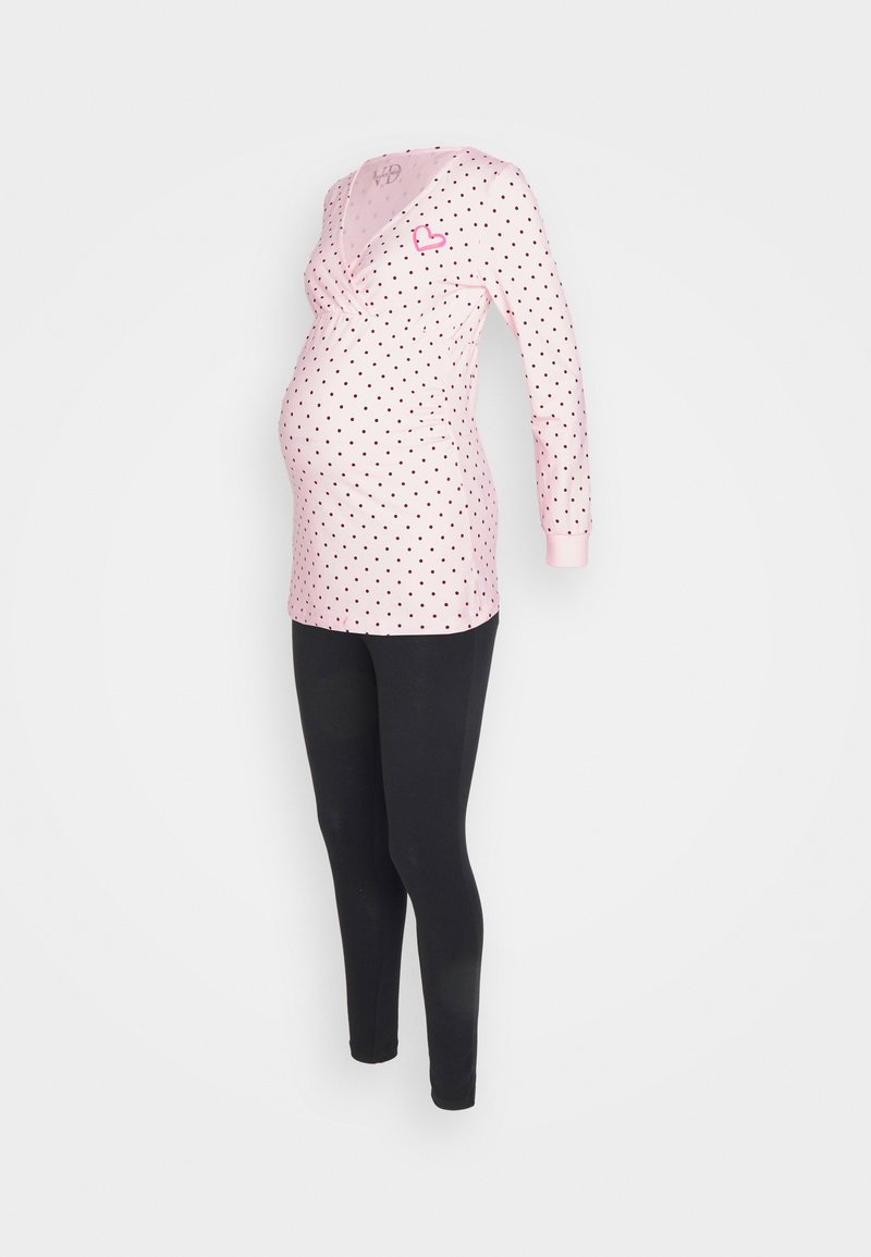 Blusa de maternidade rosa com bolinhas pretas e decote em V, combinada com leggings pretas. Apresenta um detalhe em forma de coração no peito.