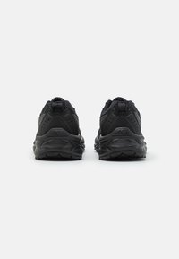 Chaussures de sport noires avec une tige en mesh texturé, un col rembourré et une semelle en caoutchouc avec un motif de traction. Vue arrière simple.