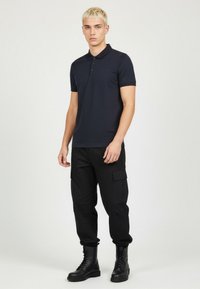 Námořnická polo tričko s třemi knoflíky, krátkými rukávy a strukturovaným povrchem, v kombinaci s černými cargo kalhotami a černými bojovými botami.