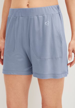 Lichtblauwe shorts met een elastische taille, voorzakken met een gebogen vorm en een klein wit logo aan de bovenkant links, gedragen door een persoon.