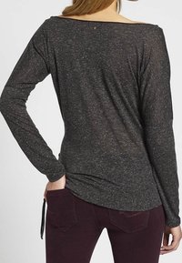 Long-sleeve, dark gray top with a loose fit and scoop neckline. Textured fabric with a subtle pattern and a small star detail at the back.