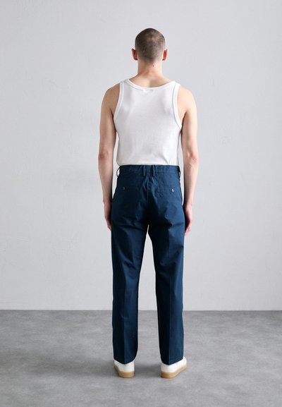 Pantalons larges bleu marine avec une texture lisse, portés avec un débardeur blanc ; dotés de poches arrière et d'une taille ajustée. Des chaussures blanches complètent le look.