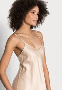 Abito slip in satin beige con spalline sottili, scollatura a V e texture liscia. Presenta una vestibilità comoda e un design minimalista.