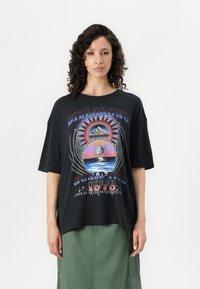 Black oversized t-shirt featuring a colorful graphic print with a sun, landscape, and text. Made from cotton with a relaxed fit.