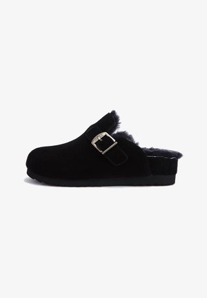Black suede clog with a fuzzy lining, adjustable buckle strap, round toe, and textured rubber sole. Simple design and clean edges.