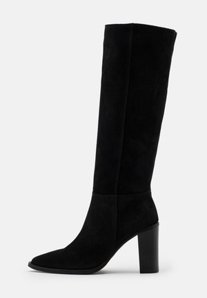 Botte noire en daim montant jusqu'au genou avec un bout pointu et un talon épais. Le design présente une texture lisse et des détails de couture minimalistes.