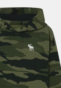 Sudadera con capucha en camuflaje verde y negro, con un pequeño logo de alce blanco bordado en el pecho.