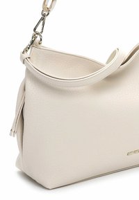 Biała teksturowana skórzana torebka z pojedynczym paskiem i kieszenią na zamek. Dno jest płaskie, z delikatnym złotym logo.