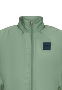 Grüne isolierte Jacke mit hohem Kragen, Frontreißverschluss und einem dunkelblauen rechteckigen Logopatch auf der Brust. Glattes, mattes Gewebe.