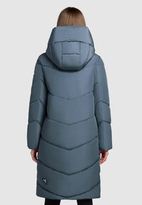 Langer, gepolsterter Mantel in einem gedämpften Blauton mit einem Zickzack-Quiltmuster und einer übergroßen Kapuze. Verfügt über ein Etikett an der Unterseite.