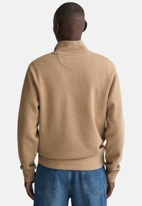 Beige trui met een hoge kraag, geribbelde manchetten en zoom. Zachte textuur en een ontspannen pasvorm, gecombineerd met blauwe spijkerbroeken.