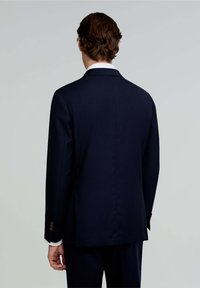 Chaqueta de traje azul marino con corte recto, solapas muesca y detalles de botones en los puños. Tejido suave con textura mínima y un diseño clásico.