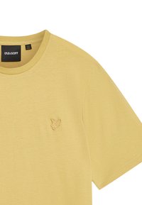 Lys gul bomulds T-shirt med rund hals, der har et lille broderet logo på venstre bryst område. Blød tekstur og afslappet pasform.