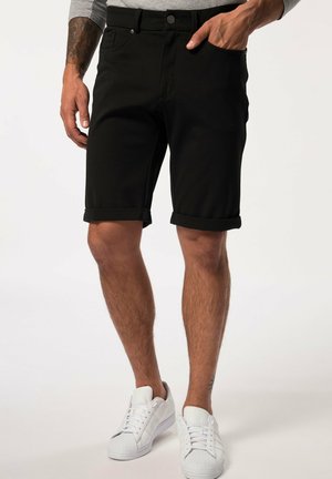Schwarze Jeans-Shorts mit umgeschlagenem Saum, klassischem Fünf-Taschen-Design und Knopfverschluss, kombiniert mit weißen Sneakers.