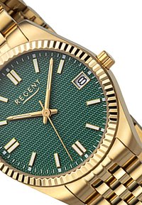 Montre dorée avec un cadran texturé vert, des marqueurs horaires dorés, un affichage de la date et un bracelet en métal. Présente une lunette cannelée.