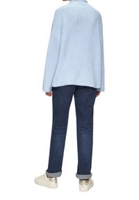 Lichtblauwe chunky gebreide trui met een hoge hals, gecombineerd met donkerblauwe jeans en witte sneakers met zilveren accenten.