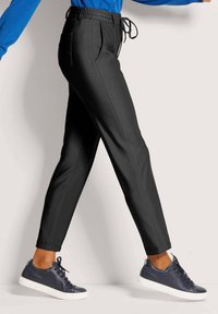 Zwarte tapered broek met een trekkoord in de taille, voorzien van zijzakken. Gecombineerd met donkerblauwe sneakers en een blauwe langemouwen top.