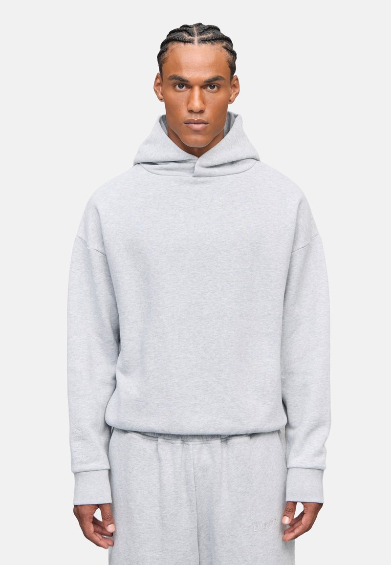 Felpa grigia con un fit rilassato, realizzata in materiale morbido. Presenta un grande cappuccio, polsini a coste e un design semplice. Nessun logo o motivo visibile.