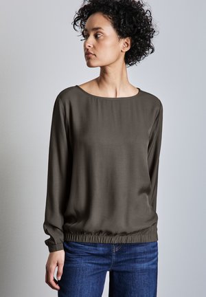 Maglietta a manica lunga di colore verde oliva con vestibilità ampia, scollatura a barca e orlo elasticizzato, abbinata a jeans blu. Tessuto dalla texture liscia.