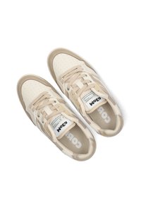 Beige sneakers with perforated leather upper, beige laces, and mesh accents. Features a white logo on the tongue and textured outsole.