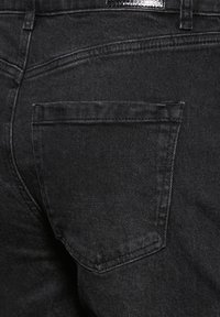 Mustat farkut, joissa on yksi takatasku suorin reunoineen ja hienovaraisine ompelutöineen, esittäen sileää pintaa.