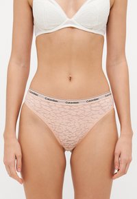 Calvin Klein csipkés bugyi selymes rózsaszínben, virágmintával, sima felülettel és fekete logóval hímzett elasztikus derékkal.