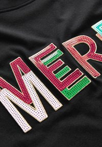 Čierna tkanina s viacfarebnými flitrovými písmenami, ktoré tvoria slovo "MERRY", s textúrovaným povrchom. Farby zahŕňajú ružovú, zelenú a bielu so zlatým prešívaním.