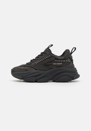 Sort chunky sneaker med tyk sål, mesh paneler, sølv nitter og "Steve Madden" branding på siden, med træksløjfer på tungen og hælen.