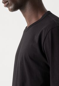 Tricou negru cu guler rotund, fabricat dintr-un material moale. Prezentând un design simplu, cu o croială lejeră și o textură netedă. Fără modele sau accente vizibile.