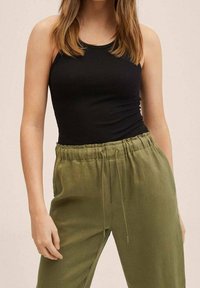 Czarny prążkowany top na ramiączkach zestawiony z luźnymi spodniami w oliwkowym kolorze na sznurek. Skupienie na dopasowanym kroju i miękkiej teksturze materiału.