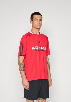 Rode Adidas sportshirt met witte accenten en logo, korte mouwen, en zwarte drie-strepen detail op de linkerschouder. Zwarte shorts.
