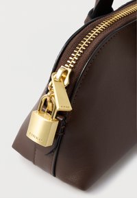 Καφέ δερμάτινη τσάντα με χρυσό φερμουάρ και υλικό κλειδώματος. Ο σχεδιασμός περιλαμβάνει δομημένο σχήμα και υφές.