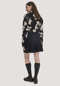 Zwarte en beige gebreide trui met een aansluitende silhouette, gecombineerd met een zwarte ribbelrok, kniekousen en zwarte schoenen.