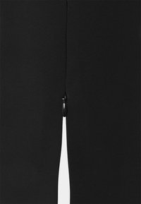 Svart kjoltyg med en mjuk textur, med en slits baktill och en liten svart dragkedjedetalj högst upp på slitsen.