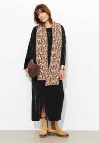 Robe maxi noire côtelée avec fente latérale, écharpe beige à imprimé léopard, pochette marron, et bottines couleur tan avec semelles noires.