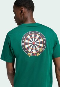 Zelené bavlnené tričko s grafikou terča na zadnej strane, s červenými, žltými a čiernymi akcentami. Krátke rukávy, bežný strih.