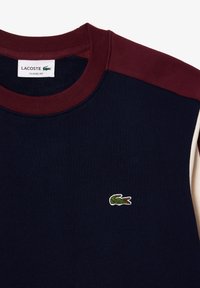 Sudadera azul marino con detalles en color granate en los hombros, cuello acanalado y logo de cocodrilo verde bordado en el pecho. Tejido de mezcla de algodón.