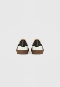 Sneakers mit weißen Lederoberteilen, schwarzen Lederakzenten an der Ferse und braunen Gummisohlen. Minimalistisches Design mit glatter Textur.