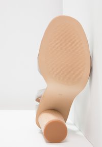 Sandalo con tacco alto grigio, con tacco a blocco in legno e suola in gomma, caratterizzato da una texture liscia e da un design con punta arrotondata.