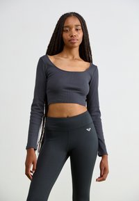 Dark gray long-sleeve crop top with a wide neckline, paired with high-waisted black leggings featuring a small heart logo. Smooth texture.