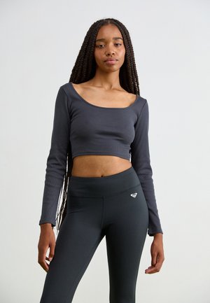 Dark gray long-sleeve crop top with a wide neckline, paired with high-waisted black leggings featuring a small heart logo. Smooth texture.