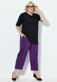 Zwarte t-shirt met korte mouwen gecombineerd met paarse panterprint broek, met een losse pasvorm en zijzakken. Model draagt zwarte ballerina's en een bril.