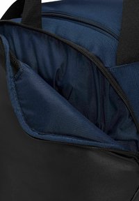 Intérieur d'un sac noir avec doublure en tissu bleu marine, fermeture éclair et texture lisse. Poche latérale avec insert en mesh pour un rangement supplémentaire.